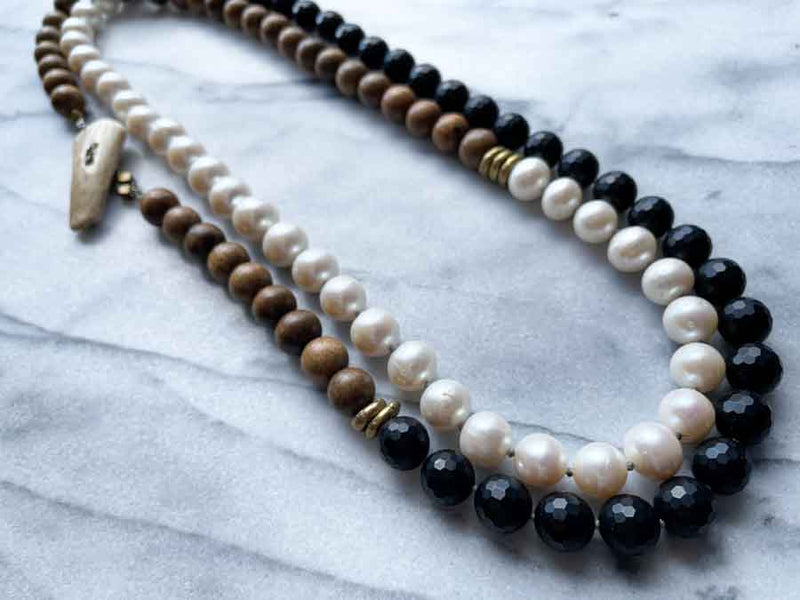 top view of gemstone bead necklace comprising white pearl, black onyx and exotic wood with antler clasp