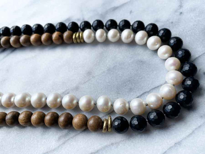 side view of gemstone bead necklace comprising white pearl, black onyx and exotic wood with antler clasp