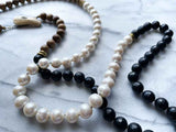 closeup of gemstone bead necklace comprising white pearl, black onyx and exotic wood with antler clasp