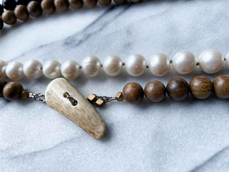 closeup of gemstone bead necklace comprising white pearl, black onyx and exotic wood with antler clasp