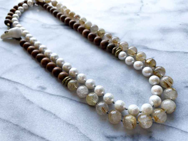 top view of gemstone bead necklace comprising white pearl, neutral rutilated quartz  and exotic wood with antler clasp