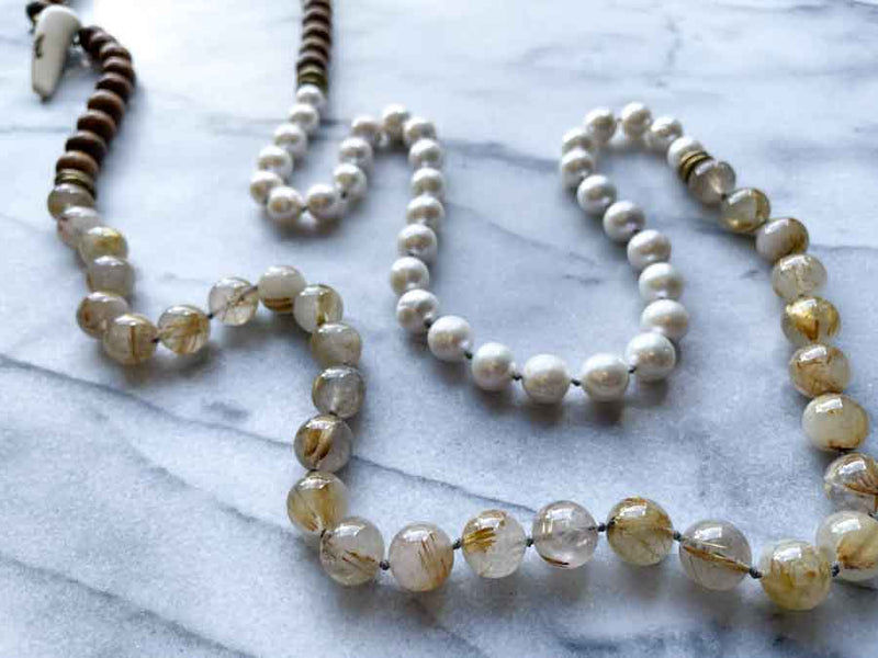 closeup of gemstone bead necklace comprising white pearl, neutral rutilated quartz and exotic wood with antler clasp