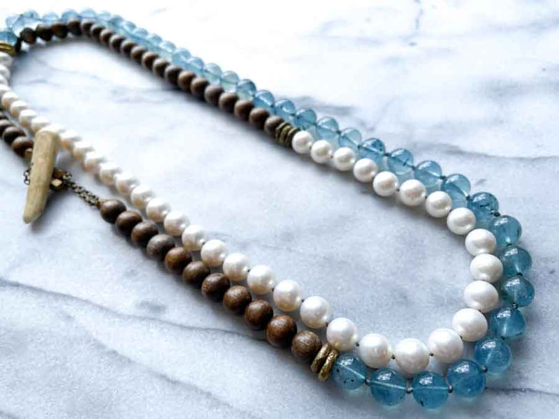 top view of gemstone bead necklace comprising white pearl, blue aquamarine and exotic wood with antler clasp