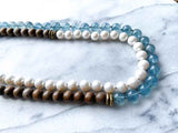 side view of gemstone bead necklace comprising white pearl, blue aquamarine and exotic wood with antler clasp