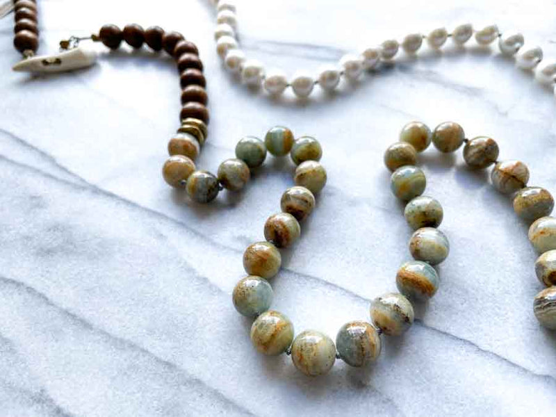 closeup of gemstone bead necklace comprising white pearl, neutral calcite and exotic wood with antler clasp