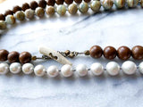 closeup of gemstone bead necklace comprising white pearl, neutral calcite and exotic wood with antler clasp