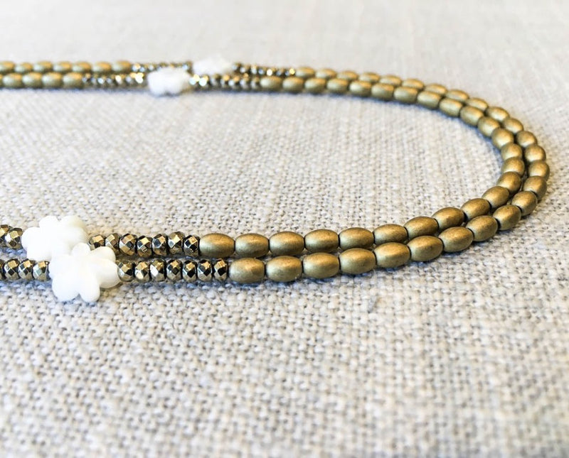 side view of gemstone bead necklace comprising carved white shell and golden metallics