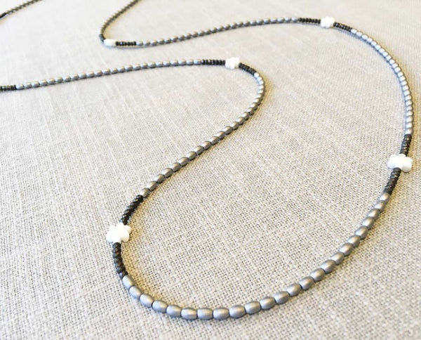 closeup of gemstone bead necklace comprising carved white shell, silver hematite and dark grey pyrite