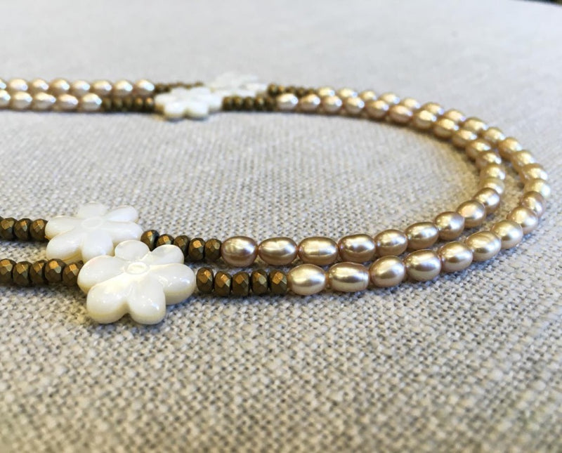 side view of gemstone bead necklace comprising carved shell, cream pearl and gold hematite