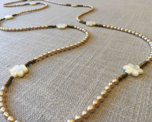 closeup of gemstone bead necklace comprising carved shell, cream pearl and gold hematite