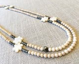 top view of gemstone bead necklace comprising carved white shell, off-white fossil jasper and dark grey pyrite