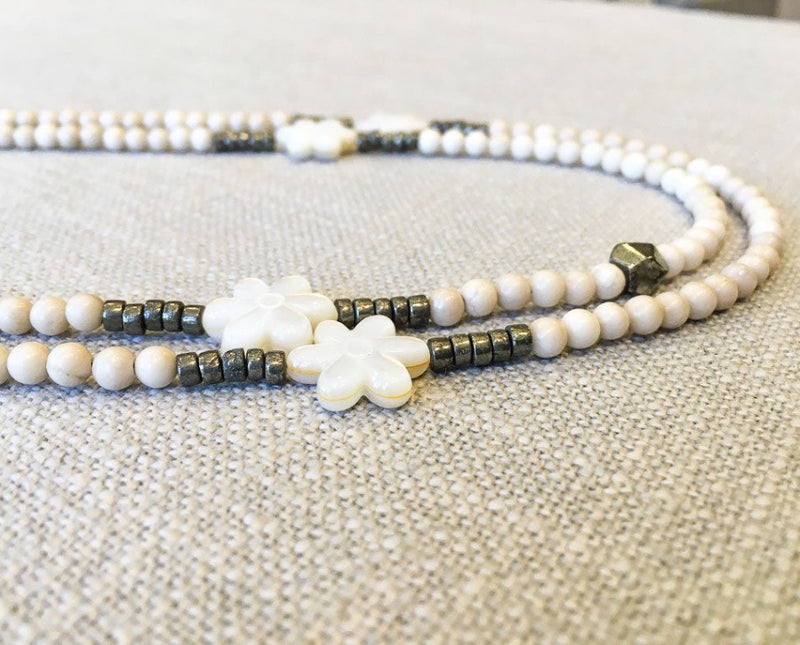 side view of gemstone bead necklace comprising carved white shell, off-white fossil jasper and dark grey pyrite