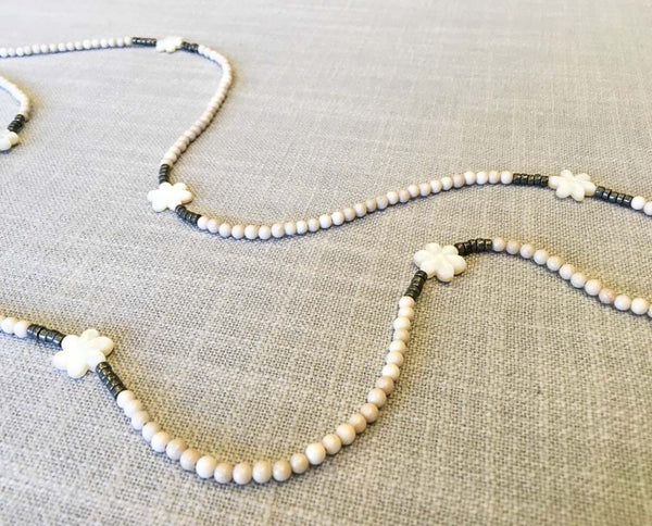 closeup of gemstone bead necklace comprising carved white shell, off-white fossil jasper and dark grey pyrite