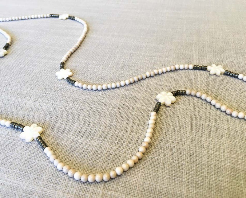 closeup of gemstone bead necklace comprising carved white shell, off-white fossil jasper and dark grey pyrite