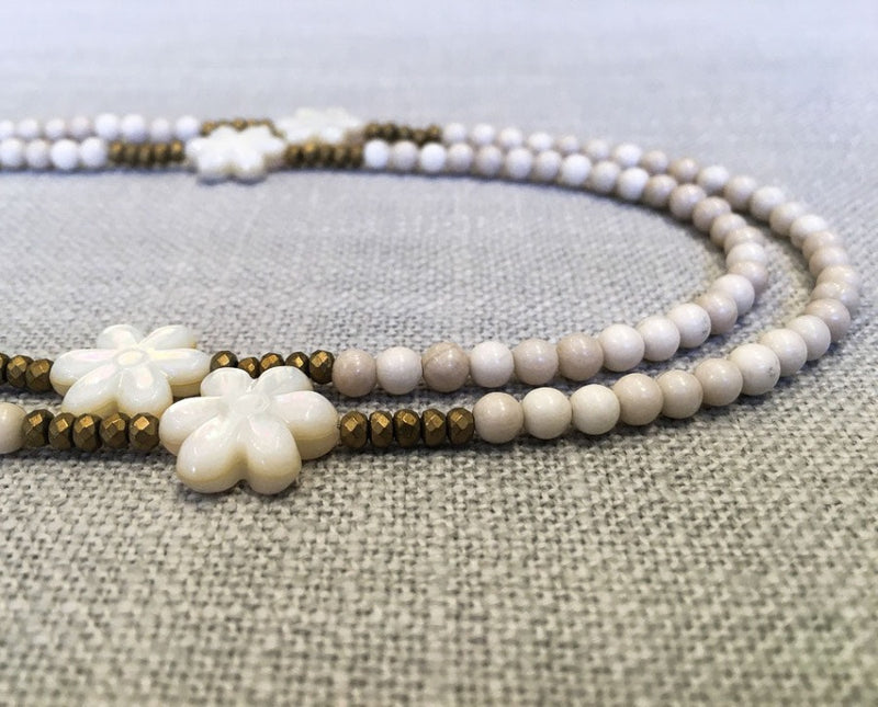 side view of gemstone bead necklace comprising carved white shell, off-white fossil jasper and gold hematite