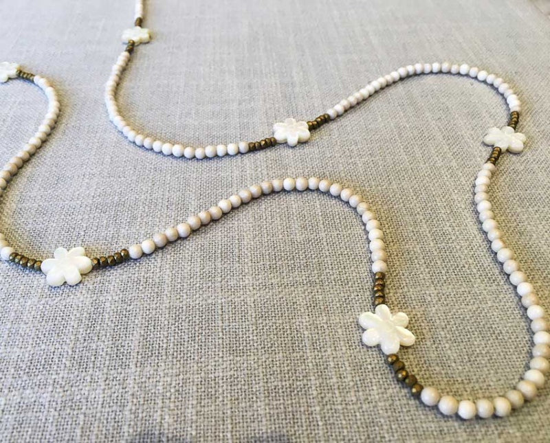 closeup of gemstone bead necklace comprising carved white shell, off-white fossil jasper and matte gold