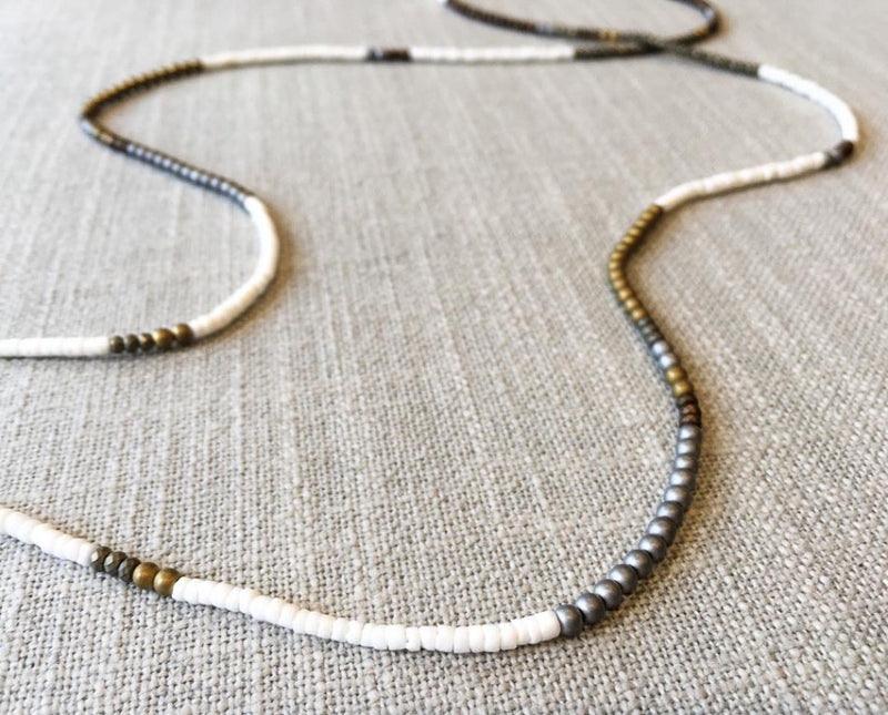 closeup of gemstone bead necklace comprising gold hematite and white shell