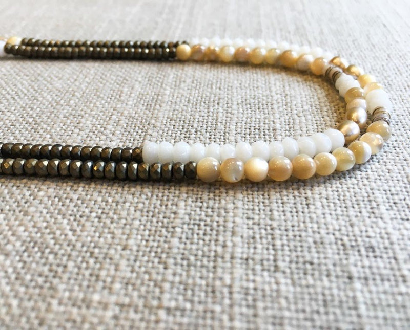 side view  of gemstone bead necklace comprising cream pearl, beige shell and light gold hematite