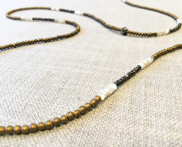 closeup of gemstone bead necklace comprising dark grey pyrite, white shell and gold hematite