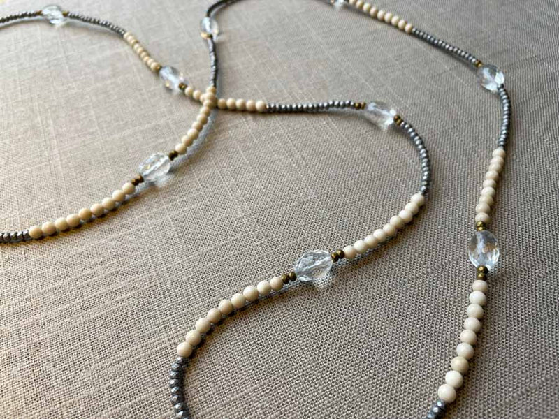 closeup of gemstone bead necklace comprising clear rock quartz, beige fossil jasper and metallics