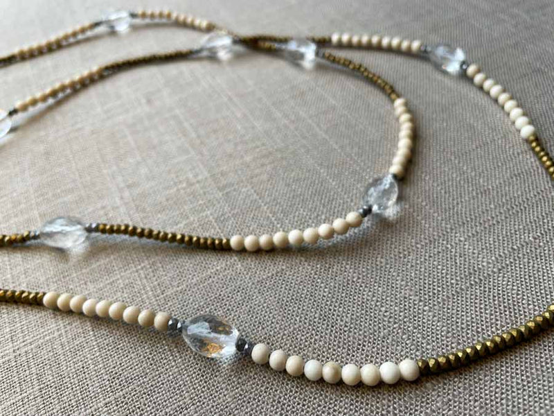 closeup of gemstone bead necklace comprising clear rock quartz, beige fossil jasper and metallics