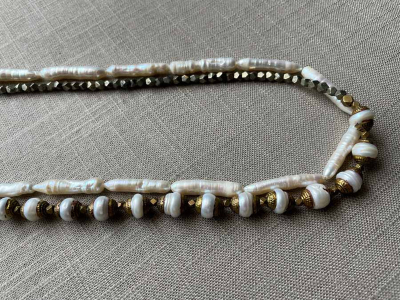 side view of gemstone bead necklace comprising white antique capped pearl, white stick pearl, dark grey pyrite