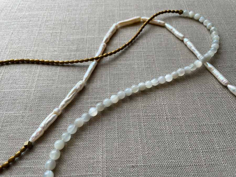 closeup of gemstone bead necklace comprising white moonstone, white stick pearl, gold hematite