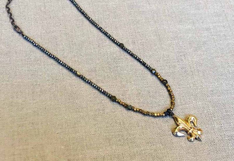 top view of antique fleur de lis pendant hung on metallic bead choker