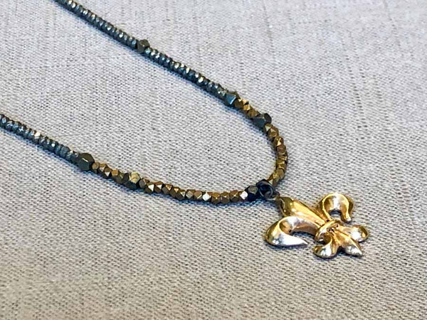 closeup of antique fleur de lis pendant hung on metallic bead choker