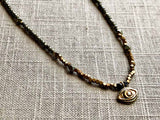 closeup of gold evil eye pendant hung on metallic bead choker