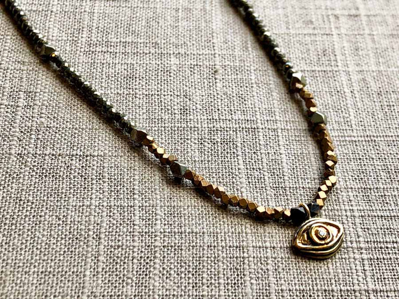 closeup of gold evil eye pendant hung on metallic bead choker