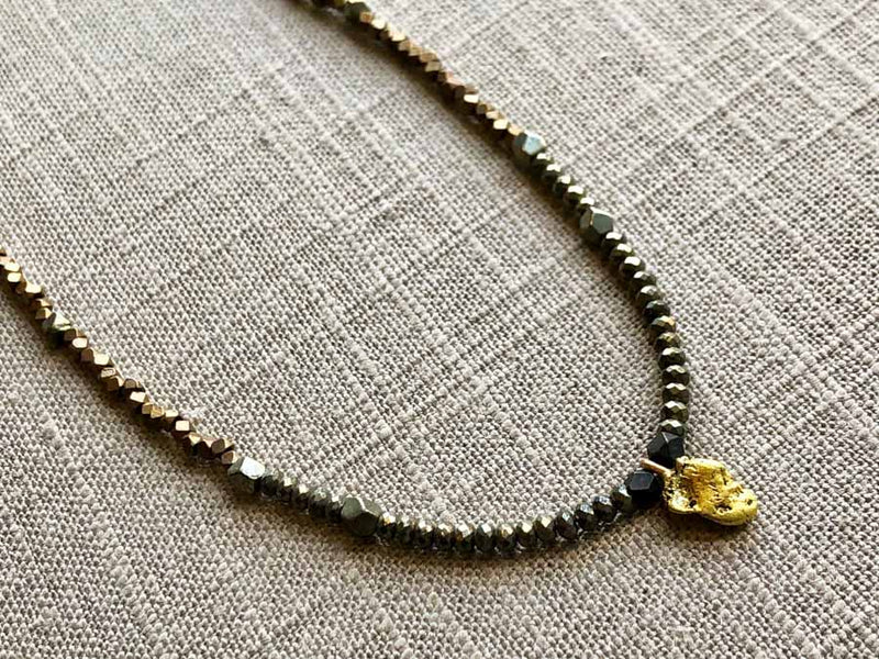 closeup of antique gold nugget pendant hung on metallic bead choker