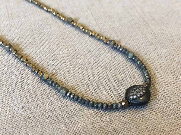 closeup of pave evil eye pendant hung on metallic bead choker