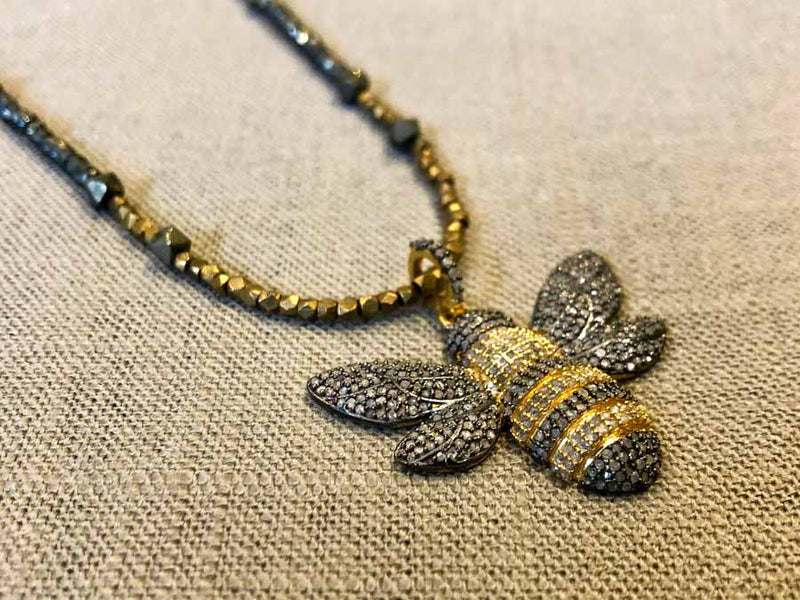 closeup of pave bee pendant hung on metallic bead choker