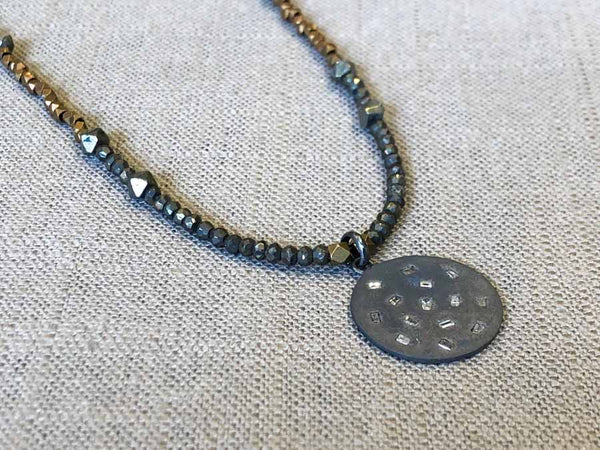 closeup of disc with diamond baguettes pendant hung on metallic bead choker