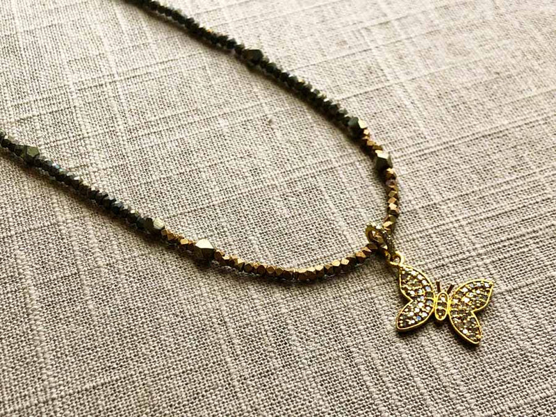 closeup of pave butterfly pendant hung on metallic bead choker