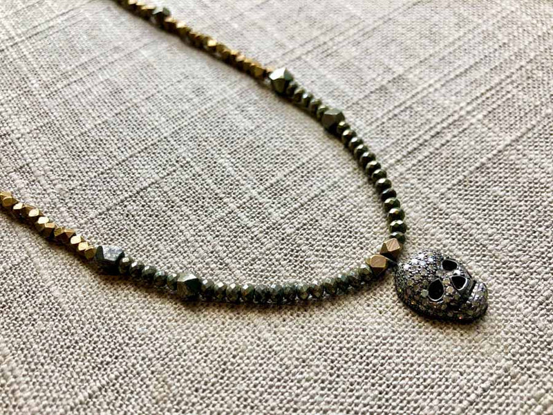 closeup of pave skull pendant hung on metallic bead choker