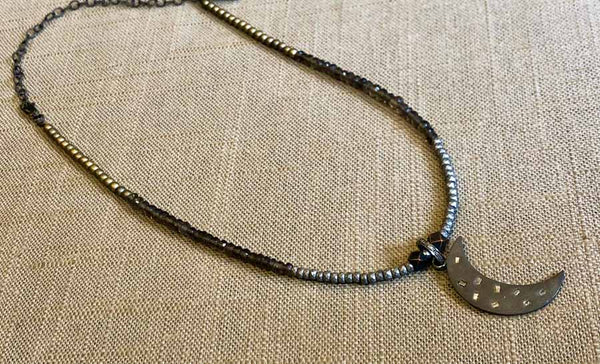 top view of pave crescent moon pendant hung on metallic bead choker