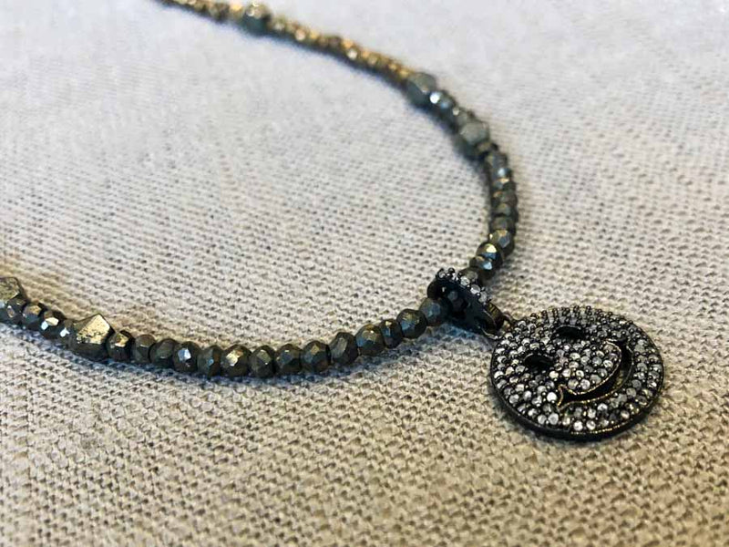 closeup of pave smiley face pendant hung on metallic bead choker