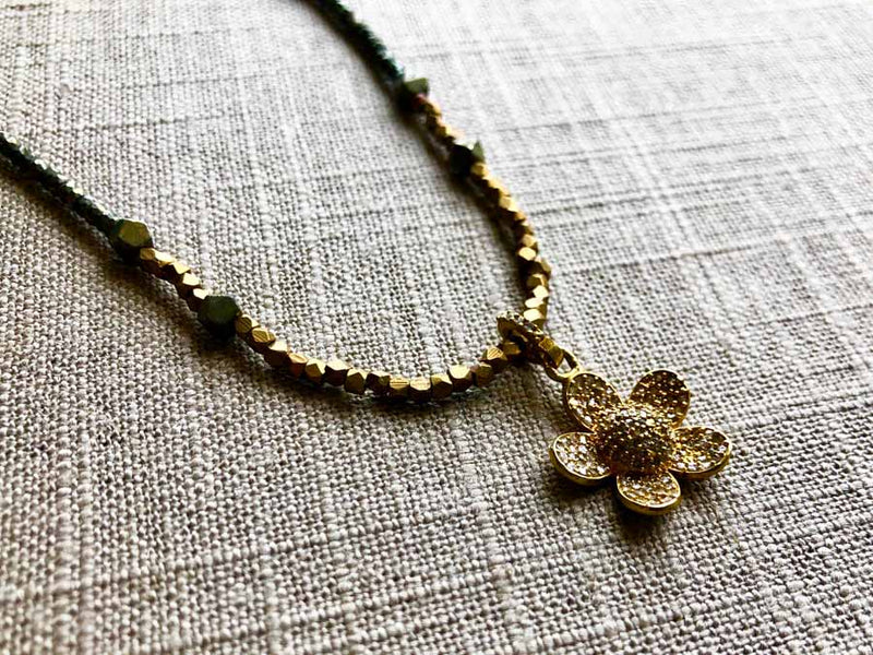 closeup of pave flower pendant hung on metallic bead choker