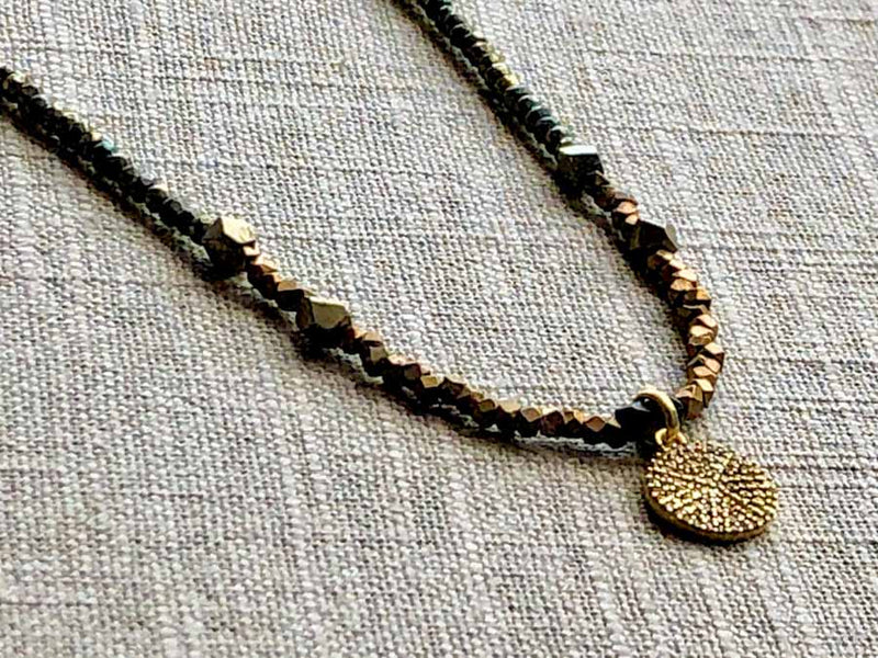 closeup of pave disc pendant hung on metallic bead choker