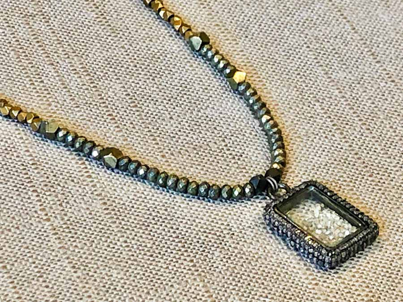 closeup of pave diamond shaker pendant hung on metallic bead choker