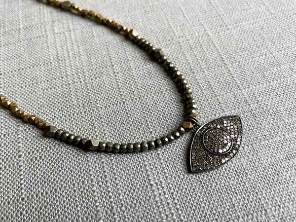 closeup of silver pave evil eye pendant hung on metallic bead choker