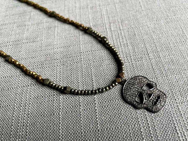 closeup of pave skull pendant hung on metallic bead choker