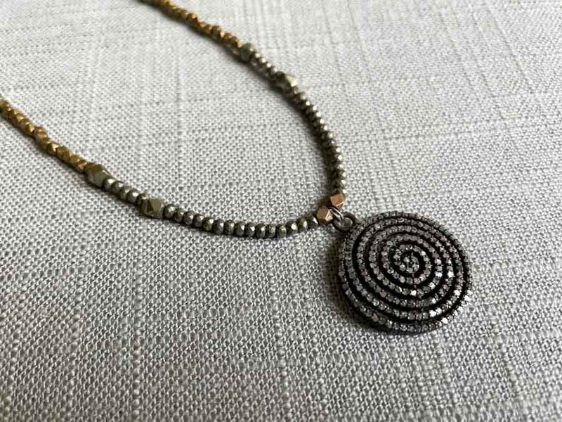 closeup of pave spiral pendant hung on metallic bead choker