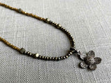 closeup of pave flower pendant hung on a metallic bead choker