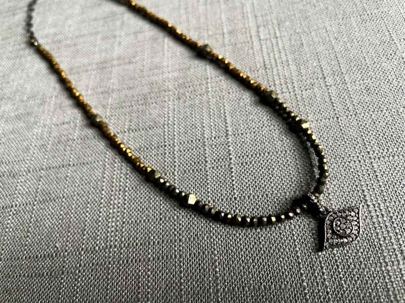 top view of pave evil eye pendant hung on a metallic bead choker