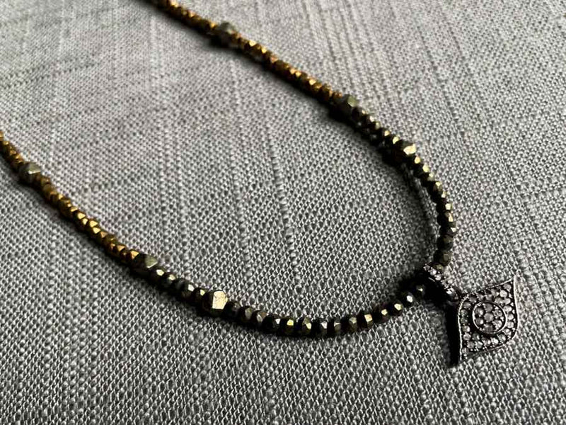 closeup of pave evil eye pendant hung on a metallic bead choker