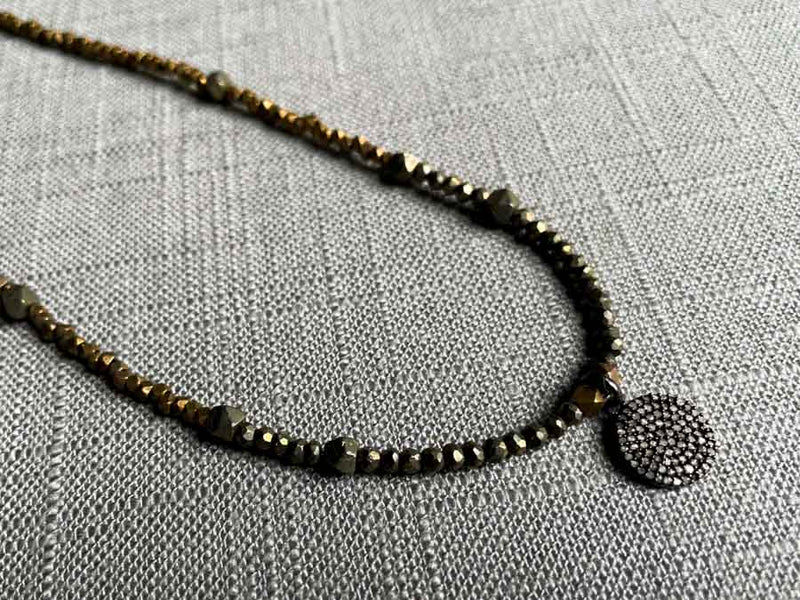 closeup of pave disc pendant hung on a metallic bead choker