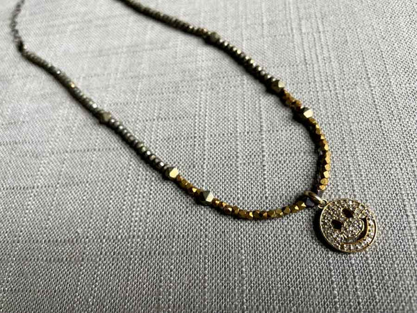 top view of pave smiley face pendant hung on a metallic bead choker